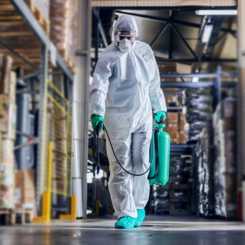 Man in protective suit and mask disinfecting warehouse full of f Man in protective suit and mask disinfecting warehouse full of food products from corona virus / covid-19.